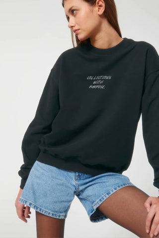 Person wearing a black sweatshirt with text and blue shorts on a white background