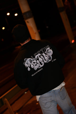 Person wearing a black quarter zip sweater with white text on the back, standing under a bridge at night