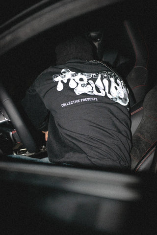 Person wearing a black quarter zip sweater with white text inside a car