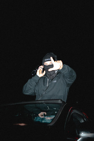 Person in dark collective quarter zip sweater with a mask calling at night while through the roof of his car.